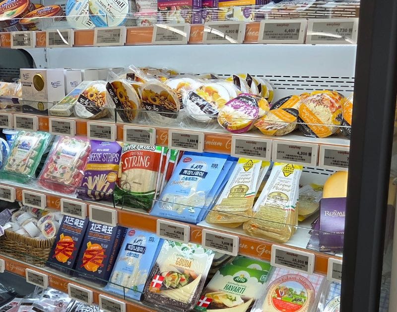 Refrigerated shelves displaying a variety of imported cheeses and dairy products.