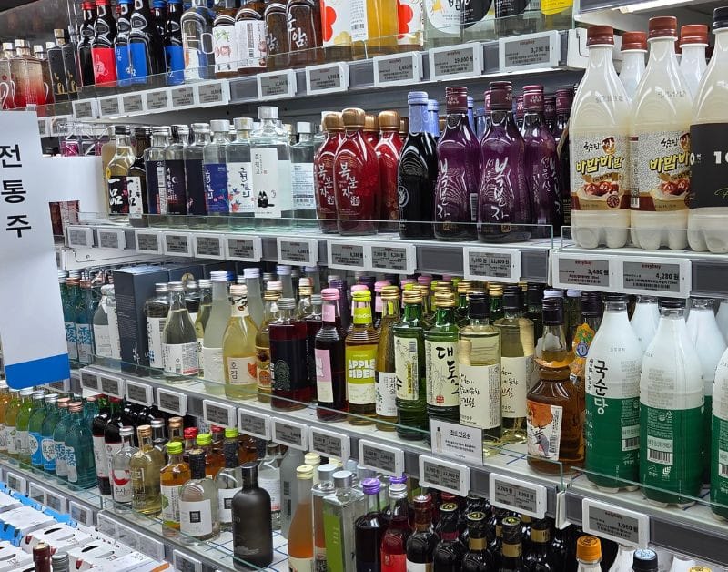 Refrigerated shelf displaying various Korean traditional alcohols like Makgeolli and fruit wines.