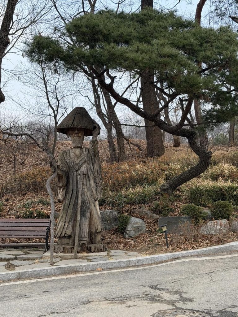 Small wooden sculpture and fine tree greets the visitors to the walk path