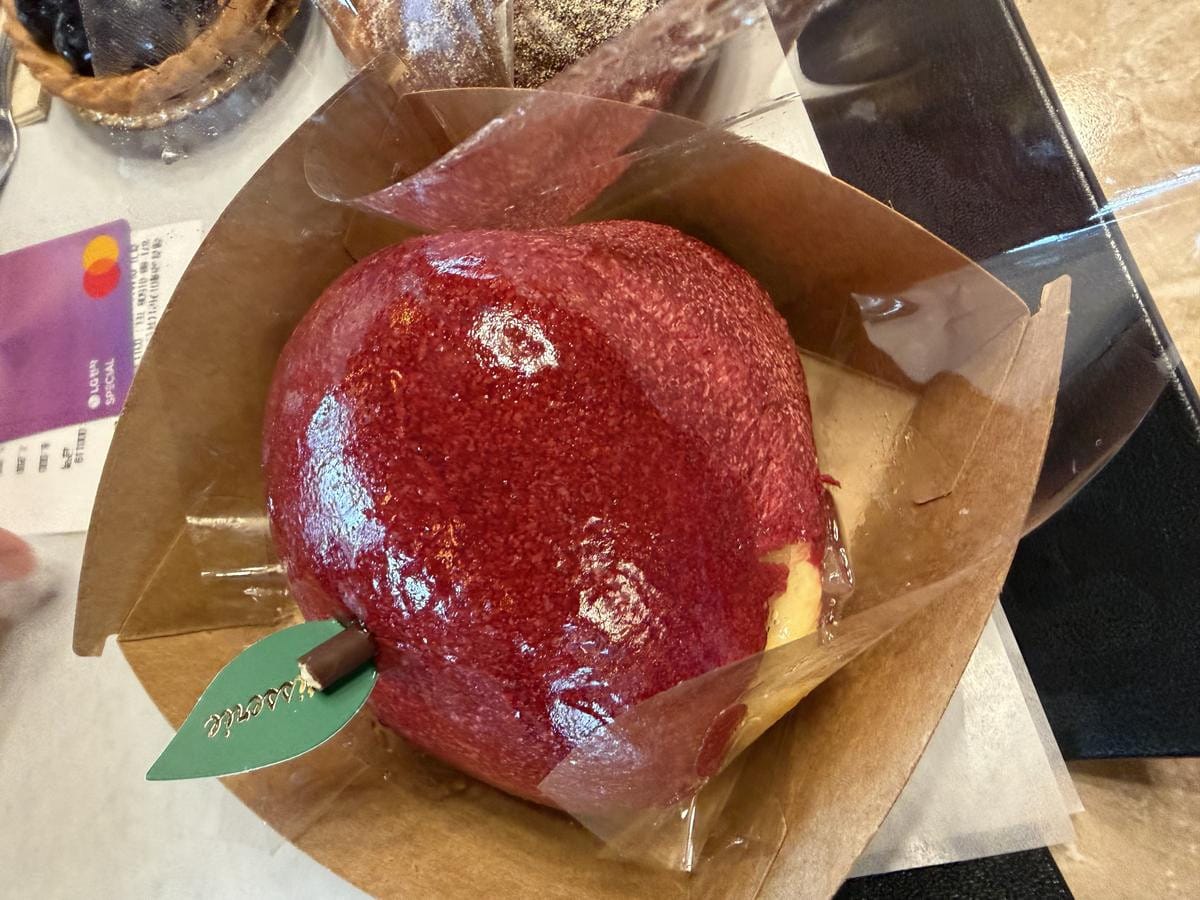 Bright red, glossy pastries shaped exactly like apples with small stems on a display tray.