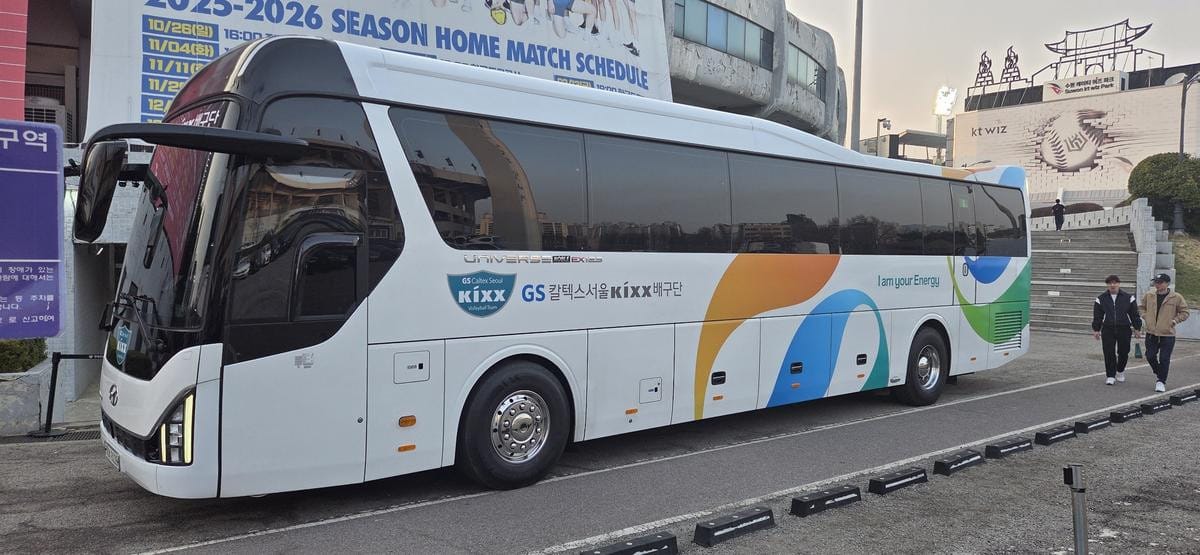 GSカルテックスのブランドロゴが入った青緑色の大型バスがスタジアムの建物の近くに駐車されている。