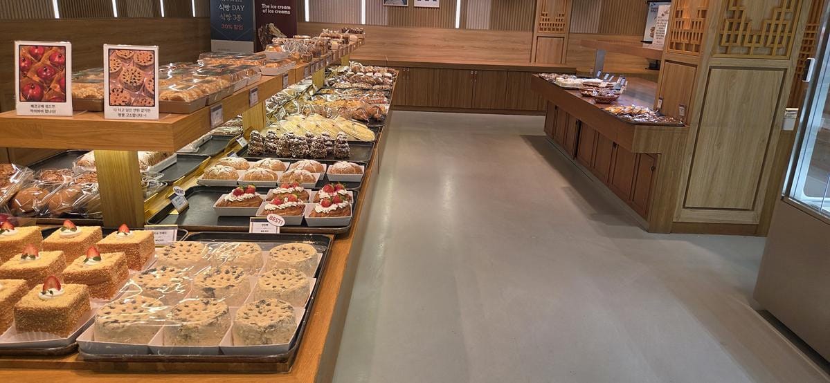 나무로 된 베이커리 진열대에 크림과 허브가 올라간 둥근 빵을 포함한 다양한 베이커리류가 놓인 모습