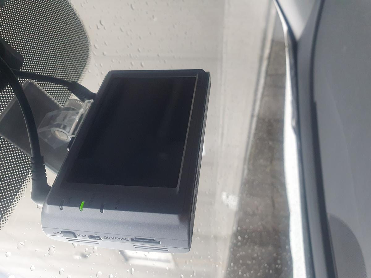 Small digital camera device mounted on the inside of a car windshield near the mirror.