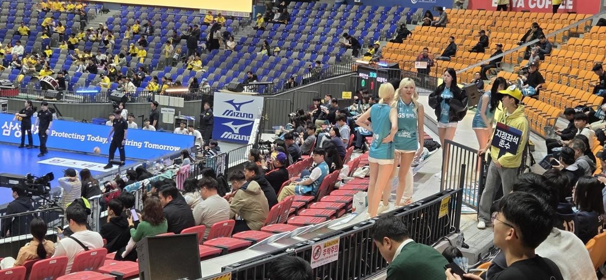 Four cheerleaders in teal and white uniforms perform on a volleyball court.