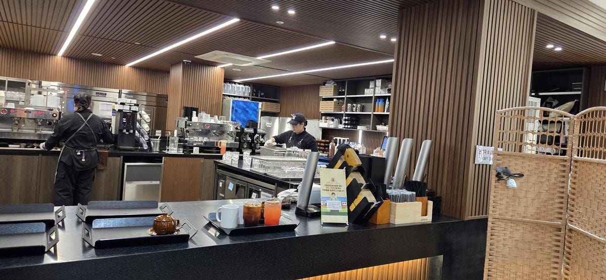 エスプレッソマシン、スタッフ、カップ、製菓機器などが並ぶ、忙しいカフェのカウンター裏の作業風景。