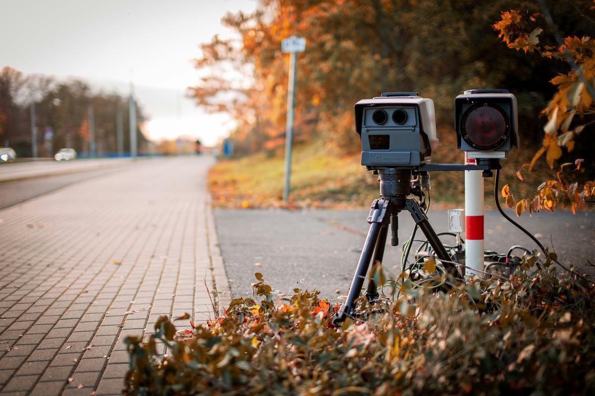 A grey speed enforcement camera mounted on a metal pole beside a paved highway.