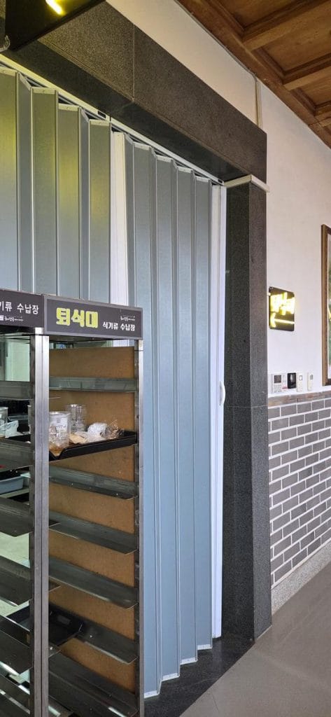 어두운 나무 수납장과 싱크대, 전자레인지, 쌓여 있는 쟁반이 있는 셀프 식기 반납대