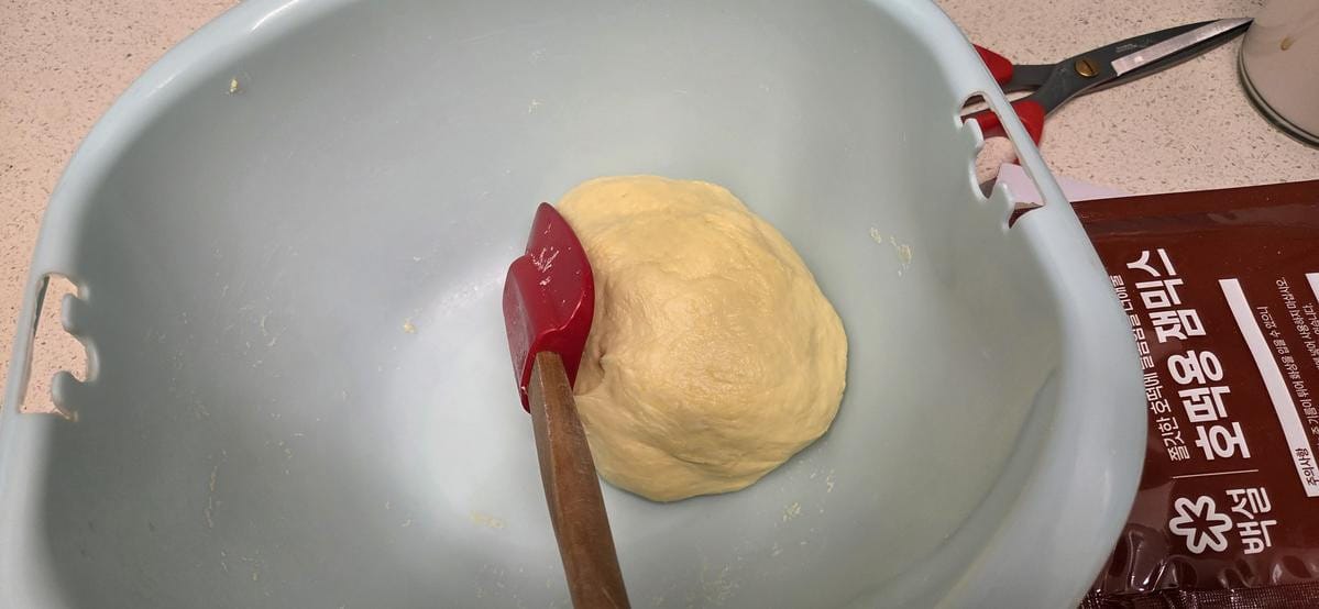 A thick, sticky pale dough mixture being kneaded inside a large round mixing bowl.