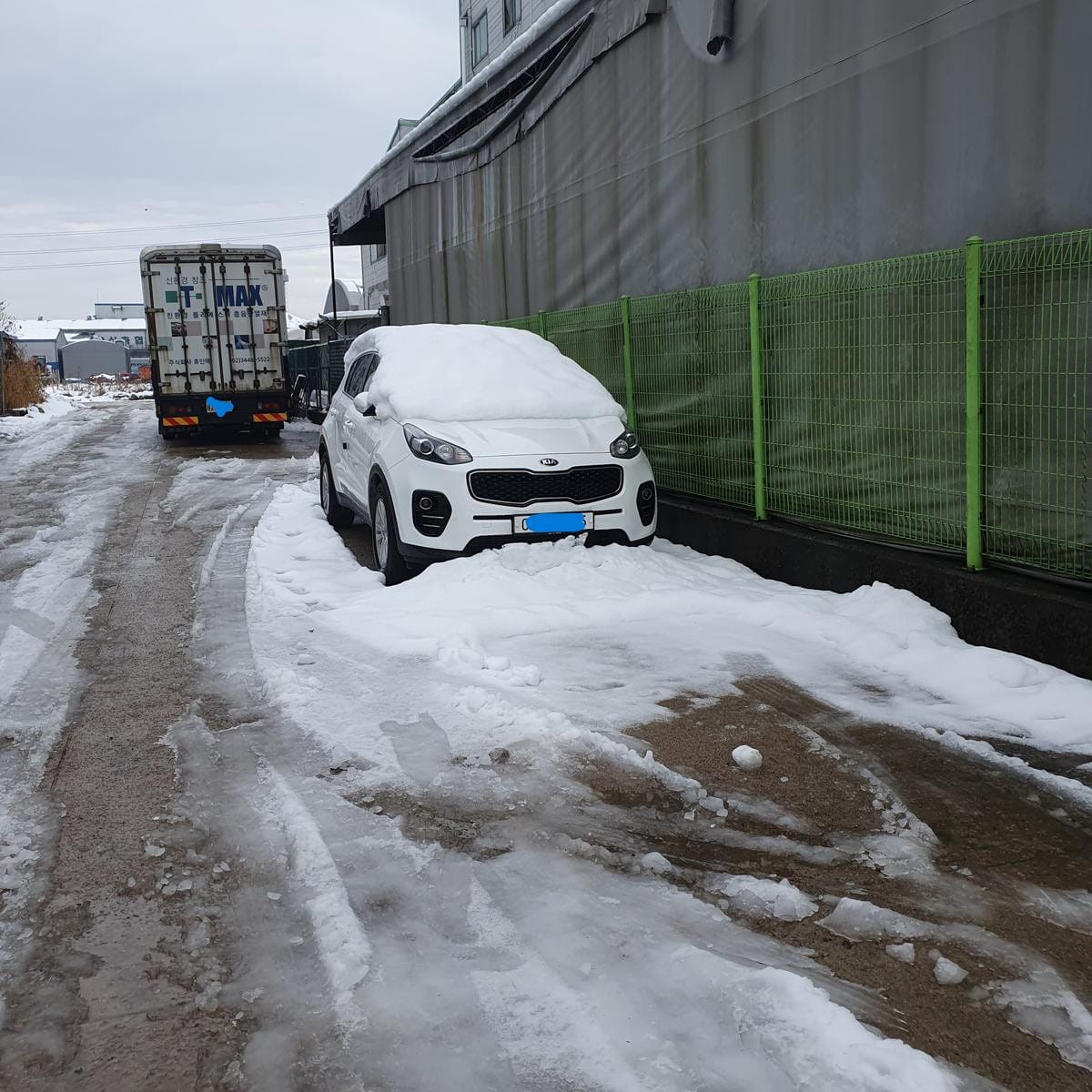 葉が落ちた木々が並ぶ歩道の横で、雪に覆われた道路沿いに駐車されている数台の車