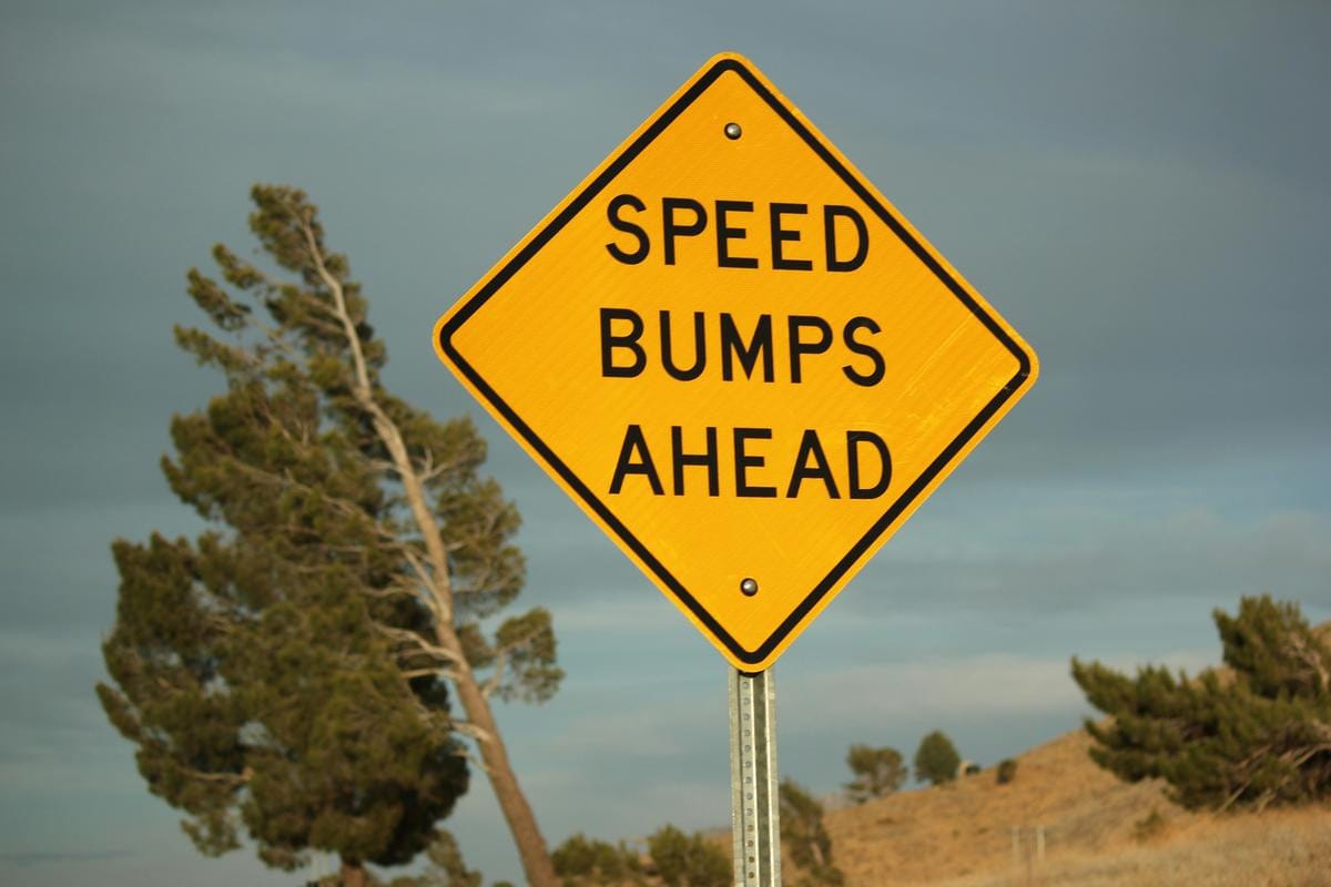 A yellow and black painted speed bump crossing an empty paved road surrounded by greenery.