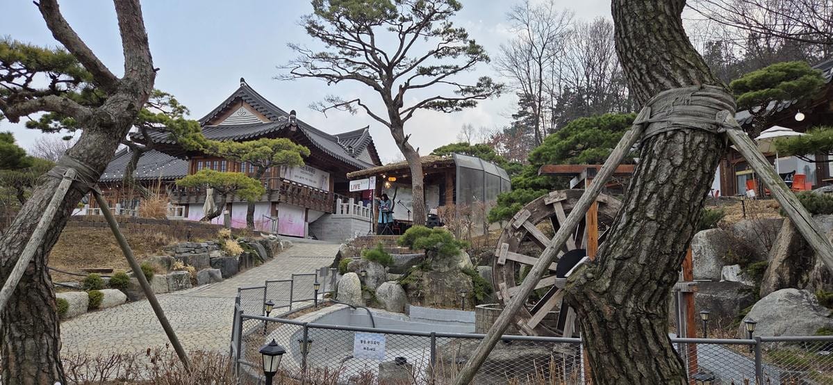 丘の上から見下ろす、伝統的な屋根の建物、石畳の中庭、木々、そして遠くの景色が広がる屋外のパノラマビュー。
