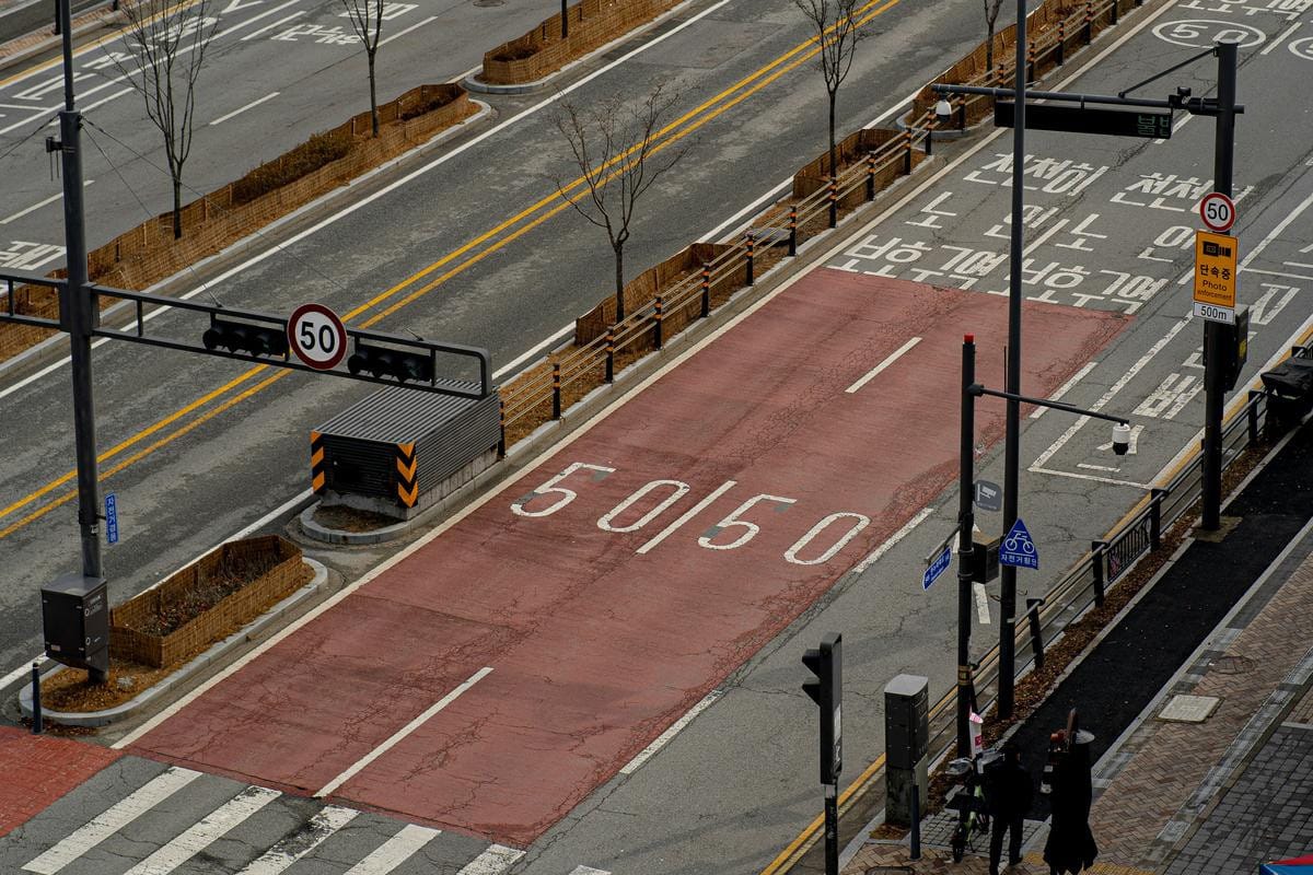 A Korean street featuring a painted safety area sign on dark red asphalt pavement.