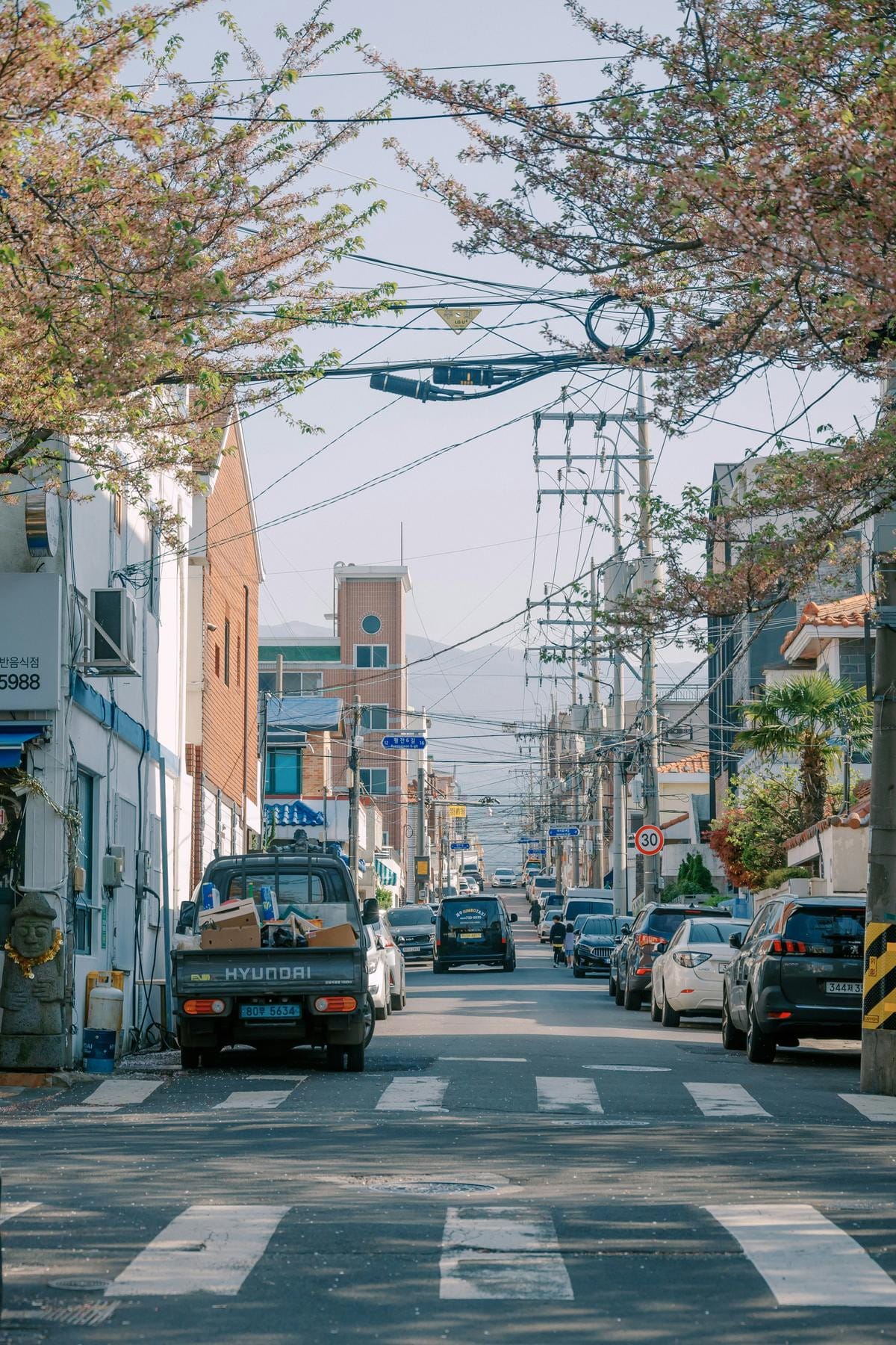 A single white sedan parked on a narrow paved street next to a tall stone wall.