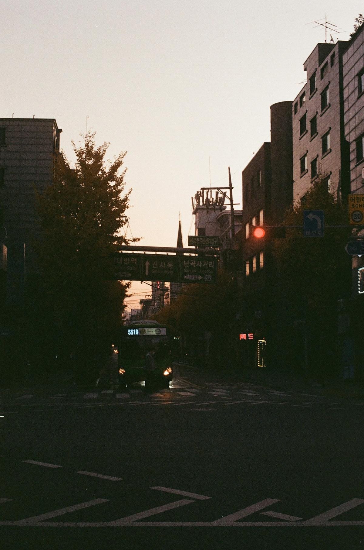 A street intersection showing a traffic light and a blue unprotected left turn traffic sign.
