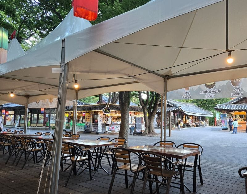 Outdoor seating area with white tents and wooden tables near the traditional food market in the Korean Folk Village.
