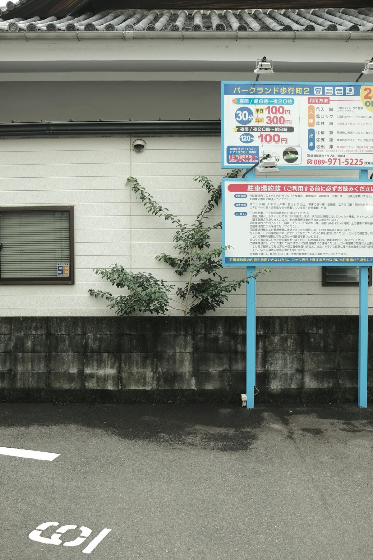 A paved outdoor parking lot with painted yellow lines, numbers, and Japanese text on ground.