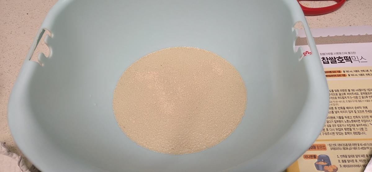 A bowl containing a cloudy liquid mixture of yeast and warm water being prepared.