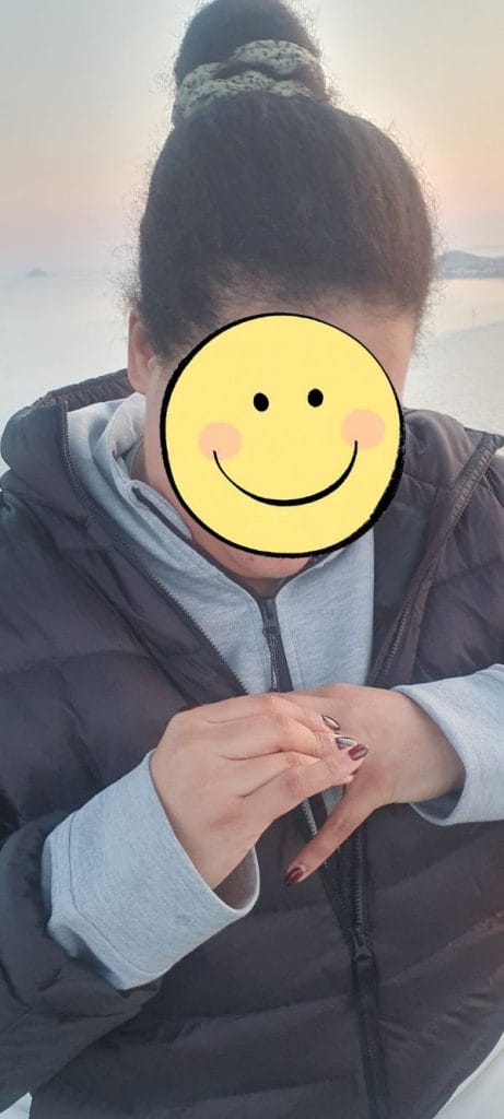 A woman smiling happily as she puts on her engagement ring inside the cable car during sunset.