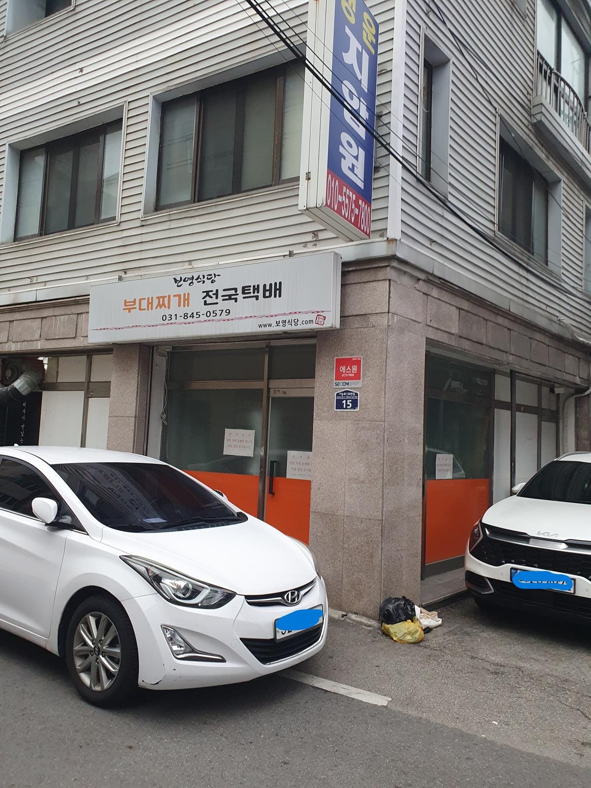 좁은 골목길 가장자리를 따라 빽빽하게 일렬로 주차된 여러 대의 차량들.