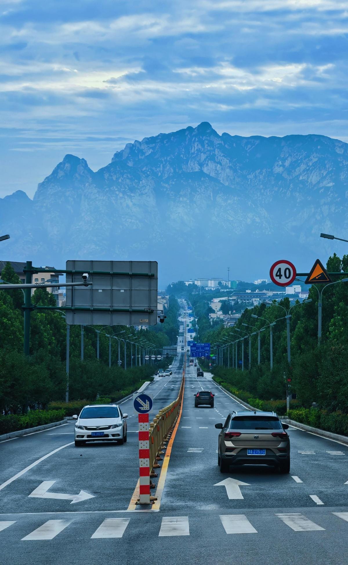 High-angle view of a dense city nestled between rolling green mountains under a hazy sky.