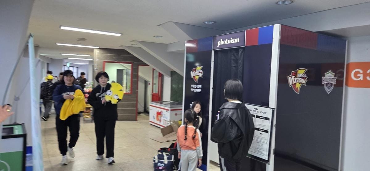People stand near two branded photo booth machines inside a building.