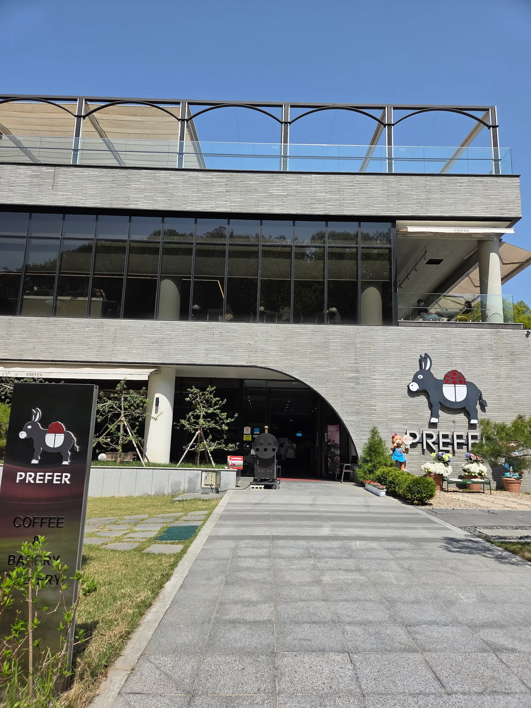 Modern grey brick exterior of Prefer Cafe in Pyeongtaek featuring a large curved window and a rooftop terrace