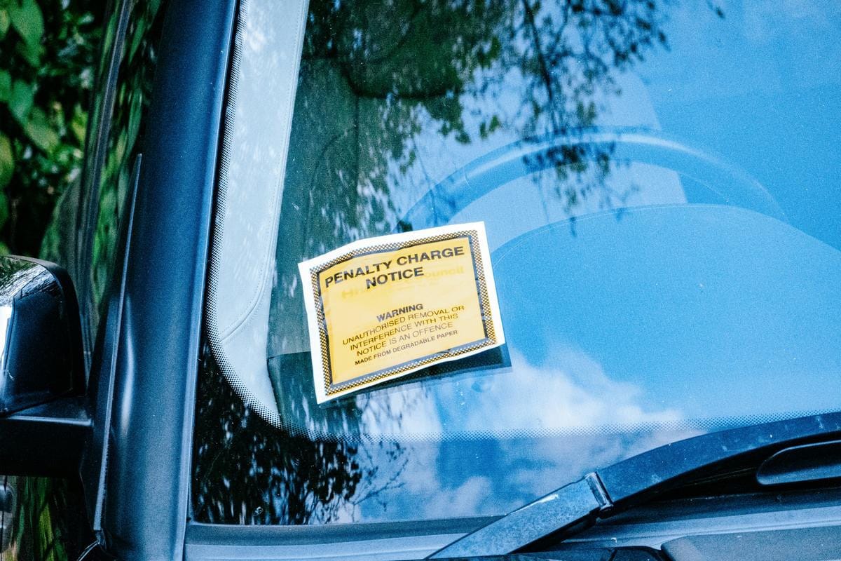 A yellow parking penalty charge notice tucked underneath the black windshield wiper of a vehicle.