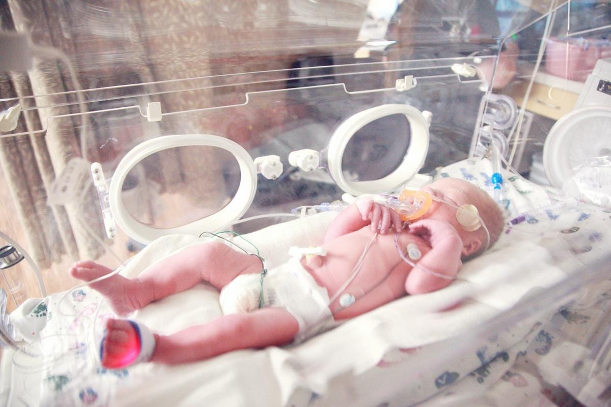 A newborn baby lies inside a transparent medical incubator.
