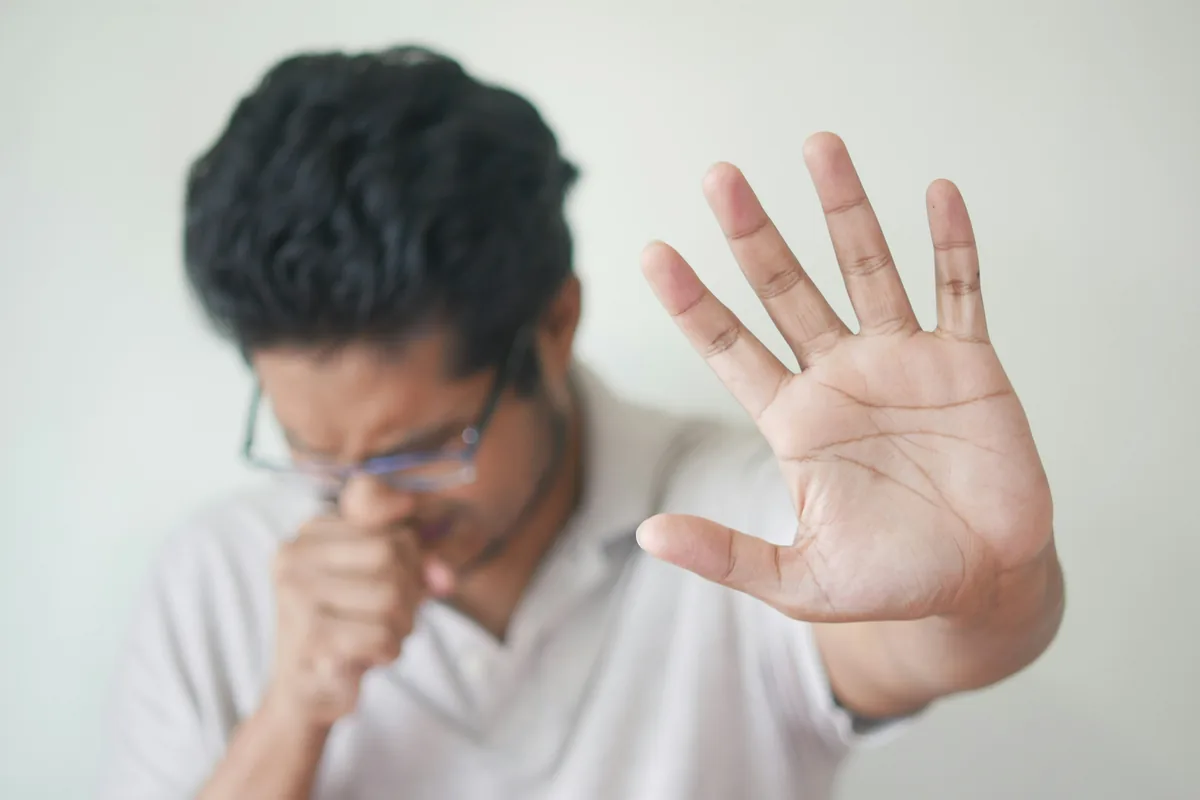 A man coughing into his hand after catching a cold during the hwanjeolgi seasonal shift in Korea.