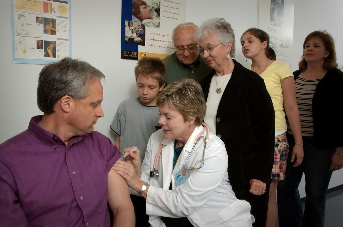 A healthcare worker wearing blue gloves administers an injection into a patient's upper arm.