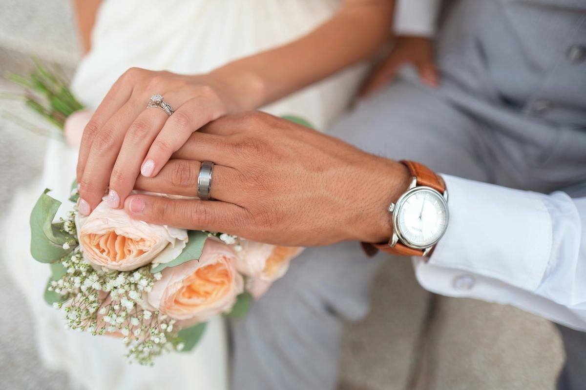 Two hands are clasped together resting on a dark surface.