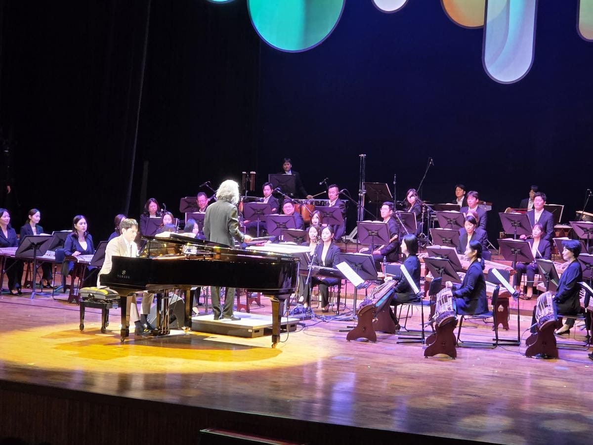 正装した音楽家たちがステージで韓国の伝統楽器を演奏しているオーケストラの公演。