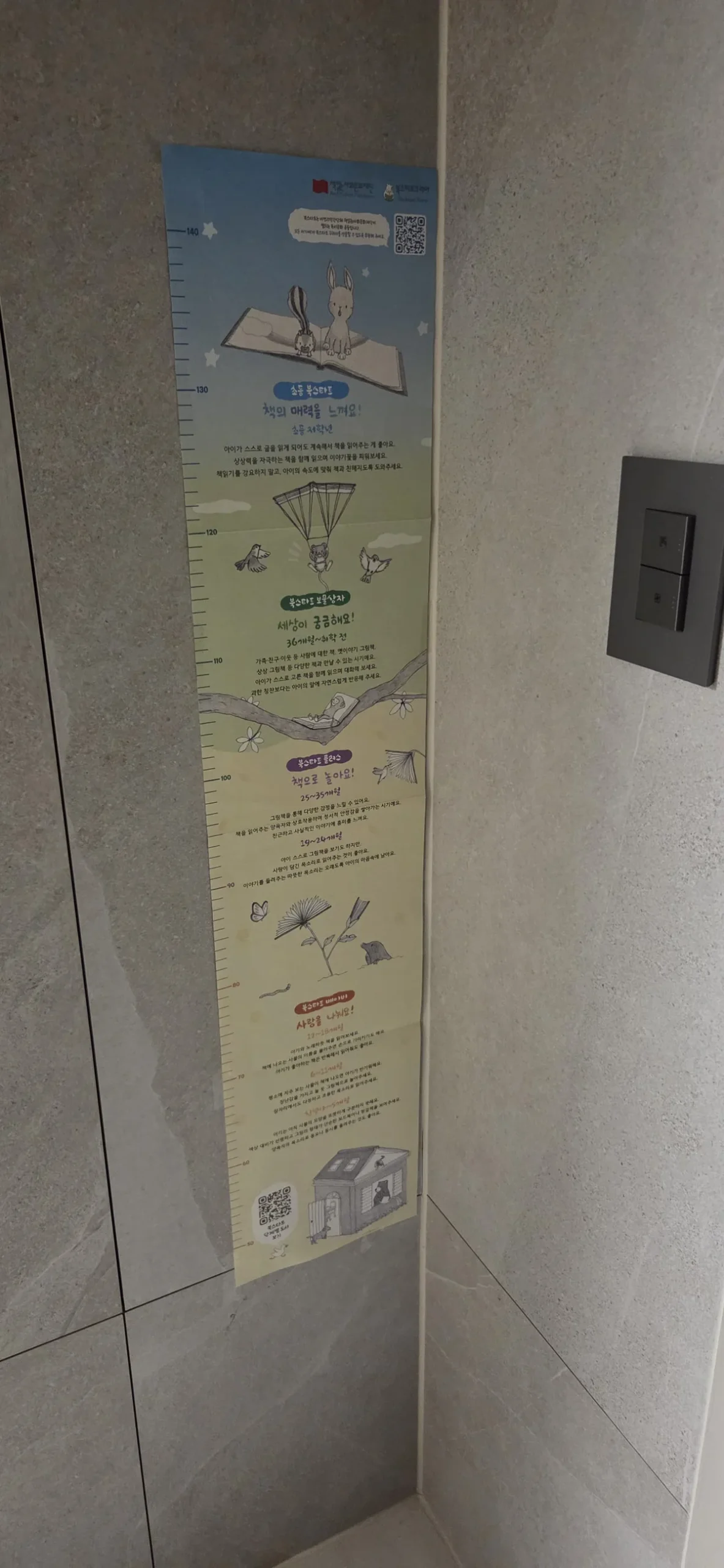 A foldable height measurement chart from the Book Start Korea book bundle contents stuck to a wall.