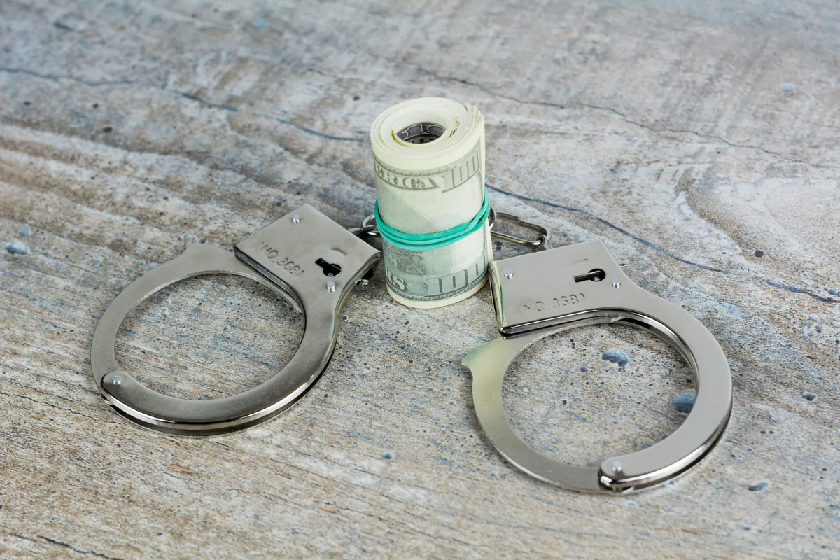 Handcuffs next to cash representing MinSik law penalties including fines up to 30 million KRW.