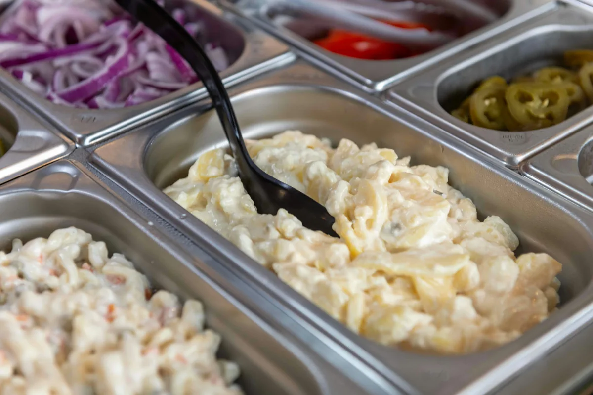 Covered buffet containers at a self-serve side dish station highlighting hygienic korean restaurant etiquette.