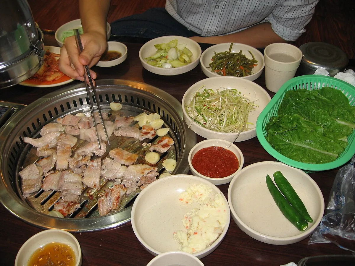 Pork belly grilling on a Korean BBQ table showing the shift to using communal tongs in modern korean restaurant etiquette.