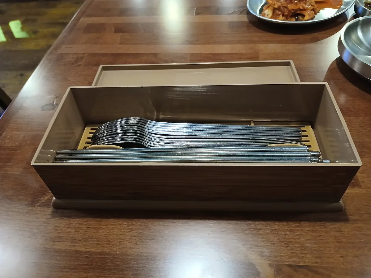 A wooden utensil box containing metal chopsticks and spoons as part of self-serve korean restaurant etiquette.