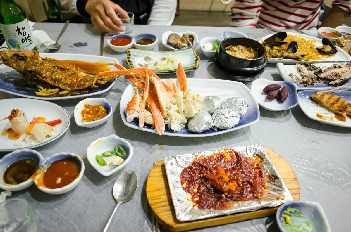 A bustling Korean restaurant table with seafood, banchan, and a bottle of soju representing the communal energy of korean restaurant etiquette.