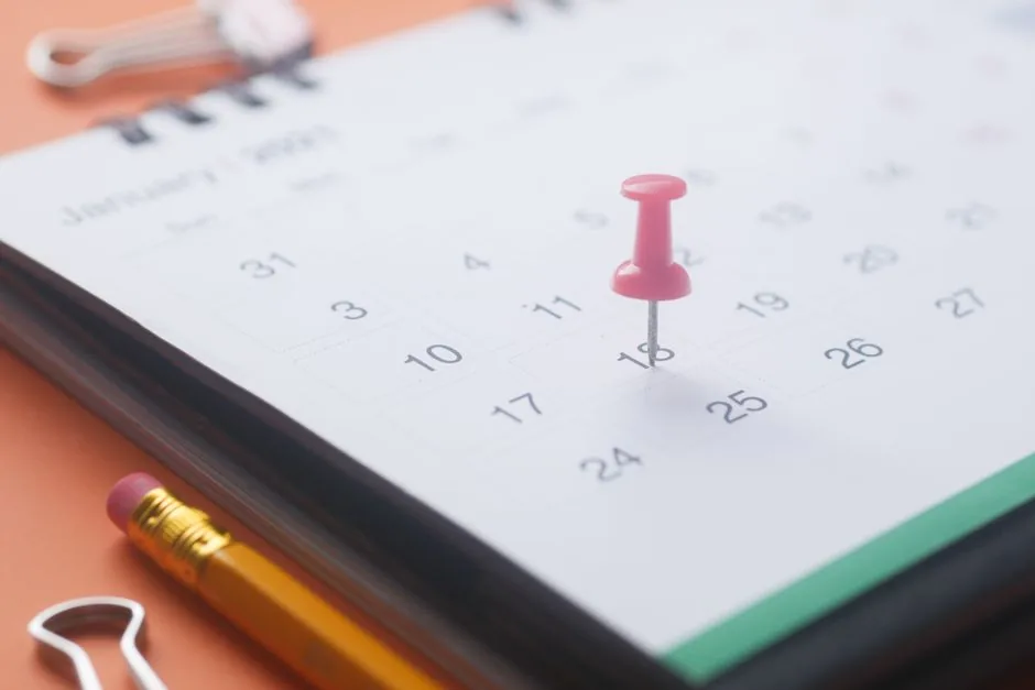 Pink pushpin marking the 18th day on an open calendar.