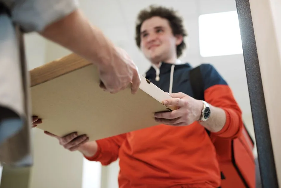 A person's hands receive a pizza box from a delivery driver.