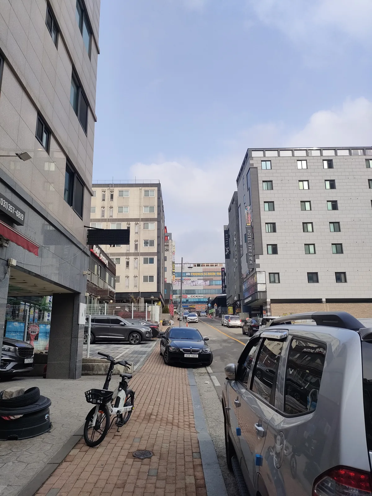 Street-level view of a Korean officetel building entrance with parked cars and bicycles on the footpath.