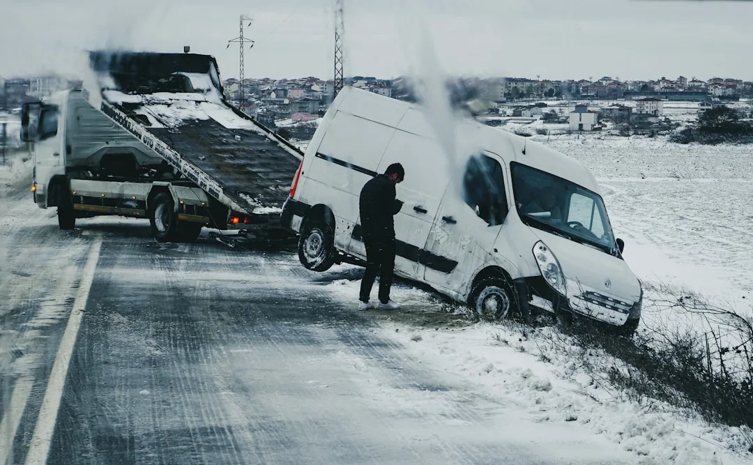 A car driving on a snowy mountain road with bare trees.