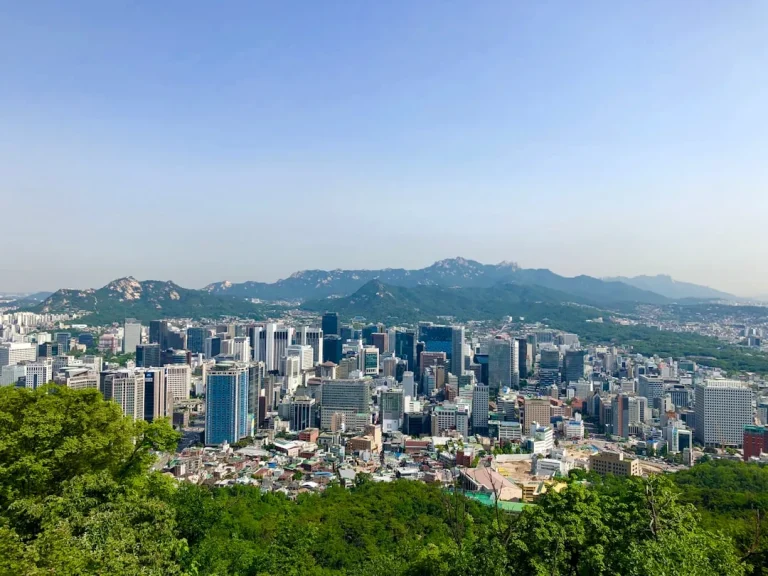 Cityscape with tall buildings and mountains under clear blue sky.
