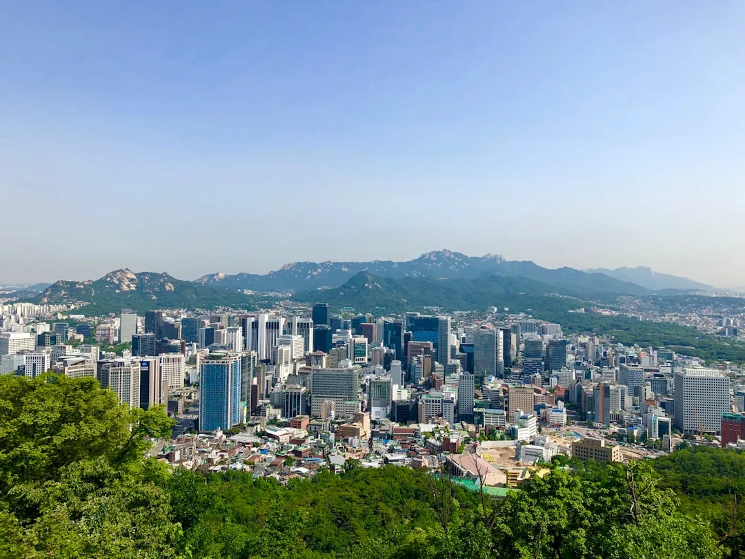 Cityscape with tall buildings and mountains under clear blue sky.