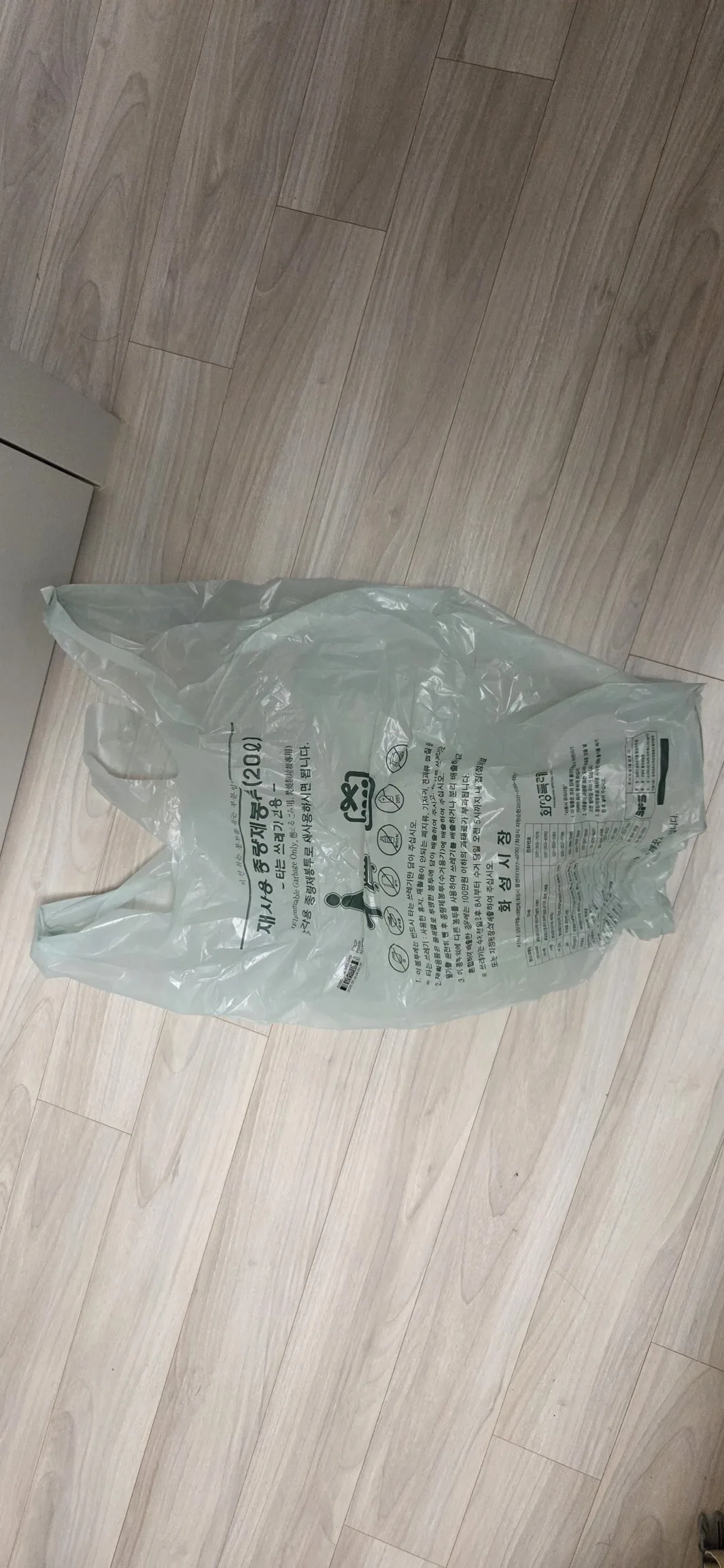 An official volume-based waste bag laid flat on a wooden floor, seen from above.
