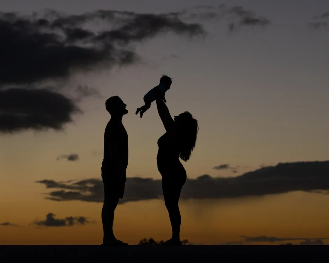 Silhouetted family with child against golden sunset sky.