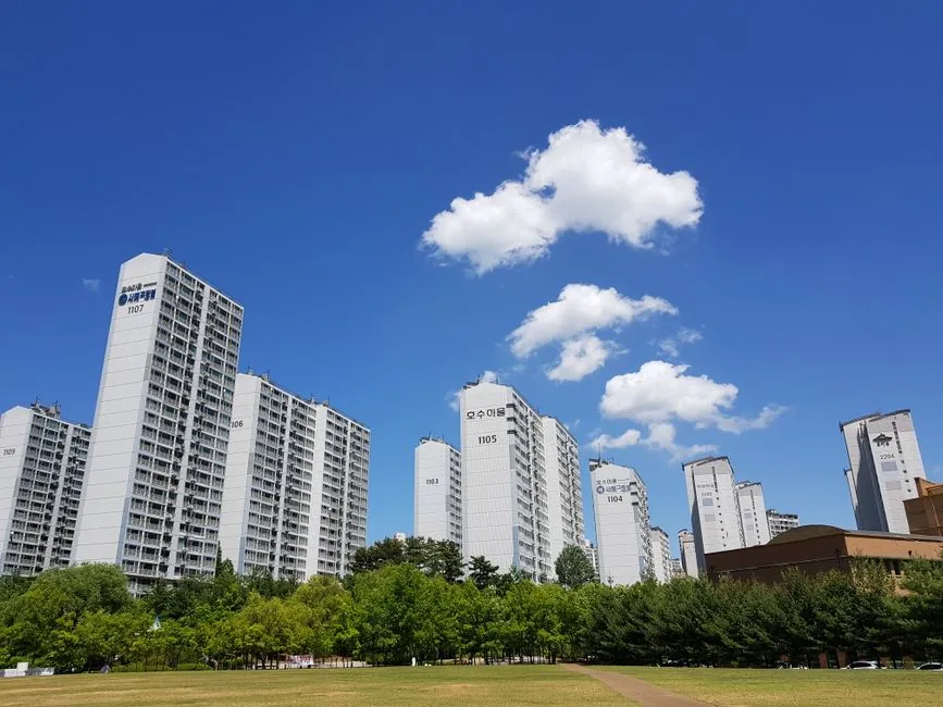 Tall white apartment buildings line a green park under blue sky.