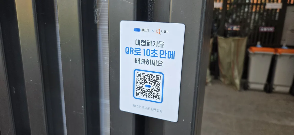 A white sign with Korean text and a QR code attached to a dark metal pole.