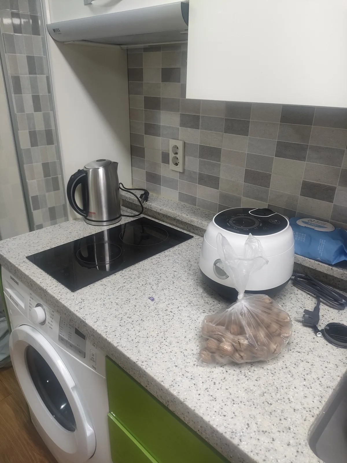 Small Korean kitchen with washing machine, induction stove, and rice cooker photographed on move-in day.