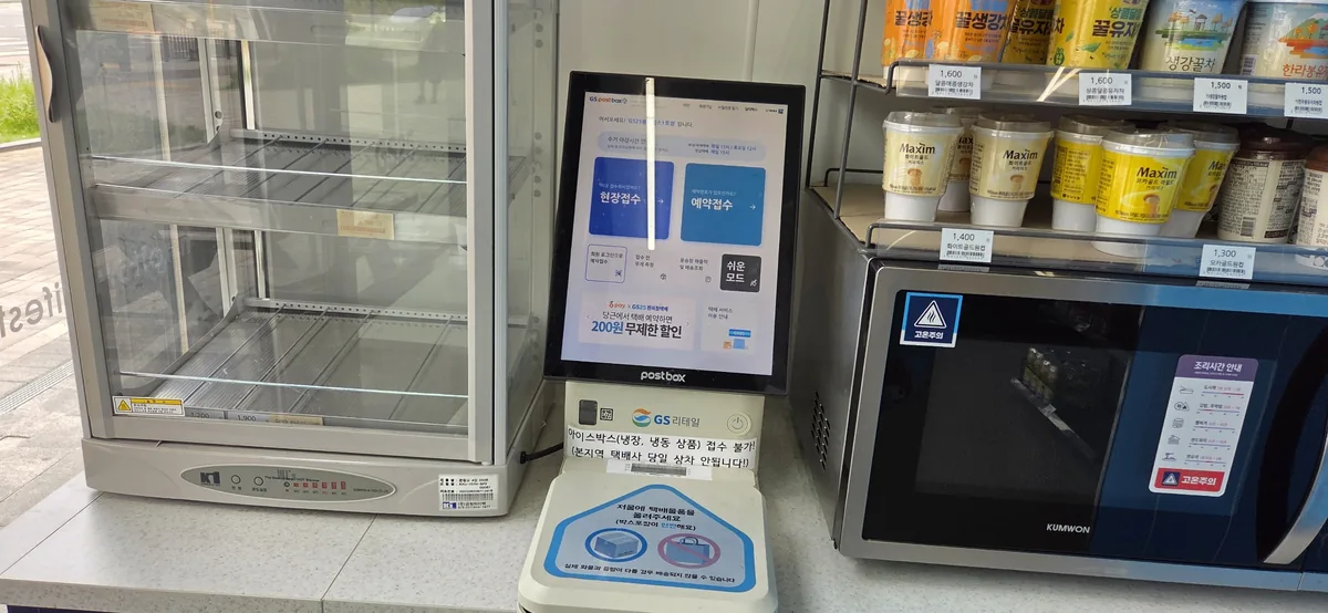 PostBox parcel kiosk with touchscreen menu displayed inside Korean convenience store.